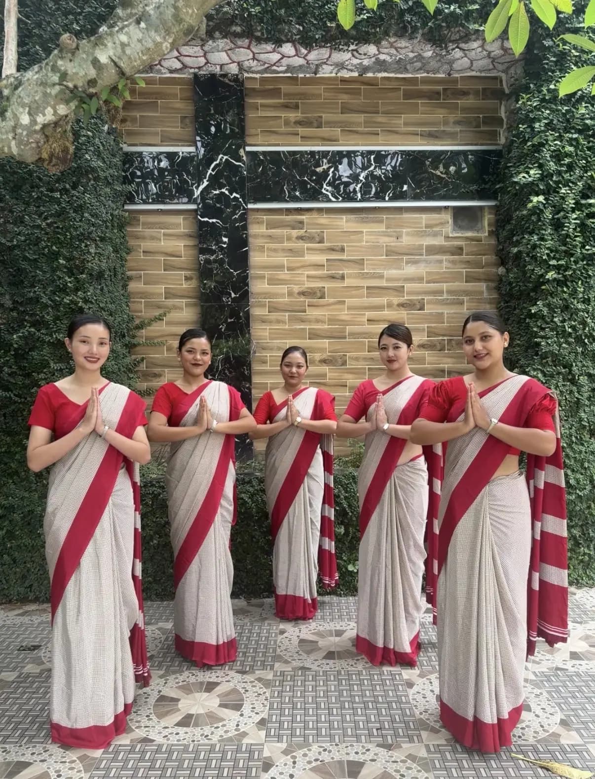 Students in red-bordered sarees greeting with a namaste